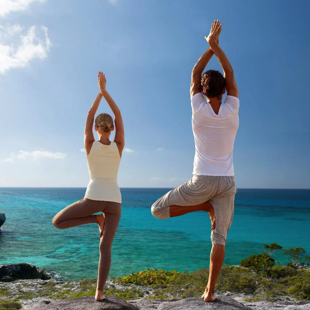 Zwei Menschen bei Yogaübungen am Meer als Symbol für einen gesundheitsbewussten Lebensstil